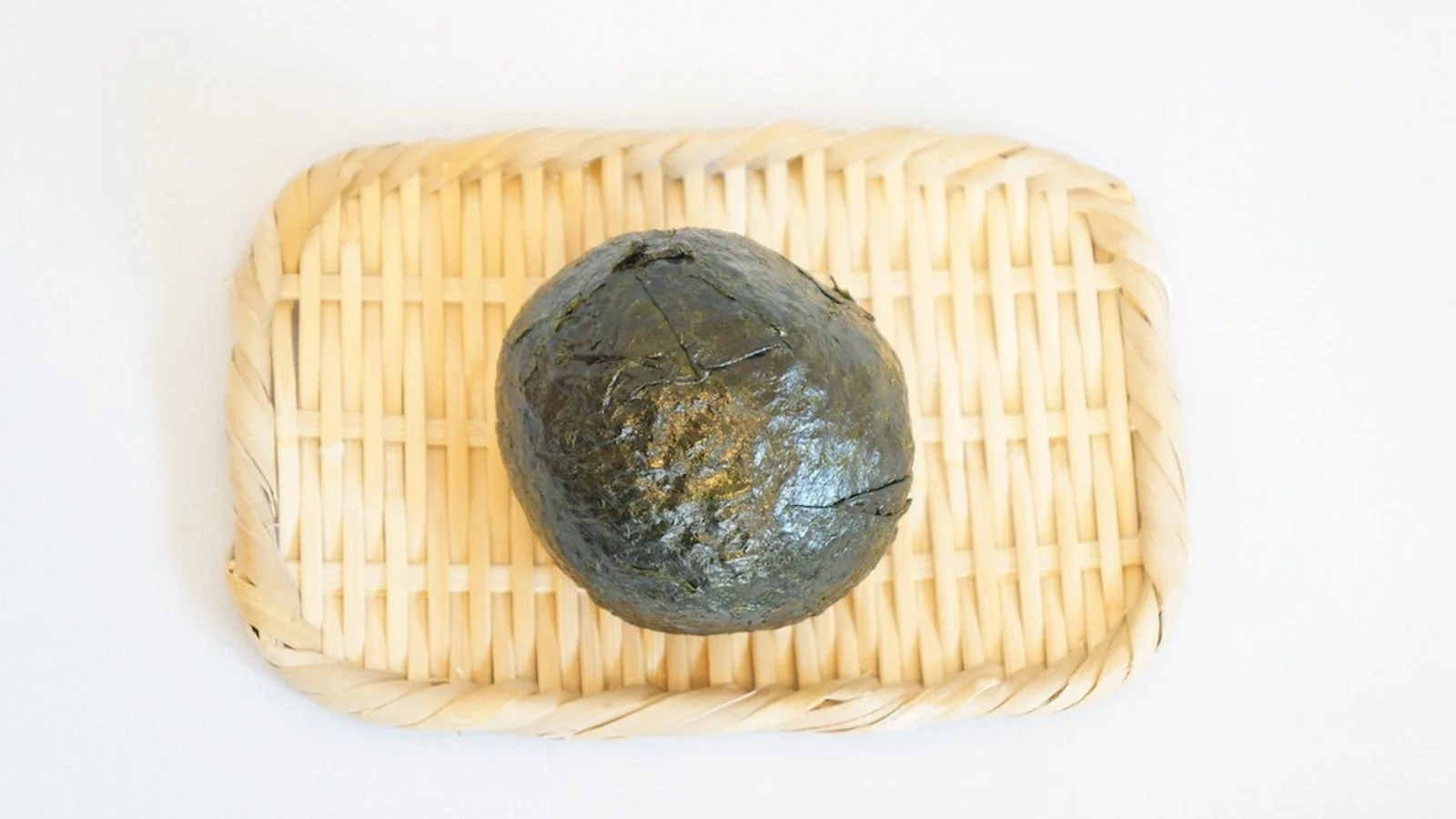 The ball fully wrapped in nori, on a bamboo tray