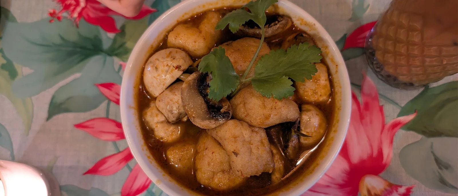 A bowl of tom yum with fried tofu and mushrooms, topped with coriander